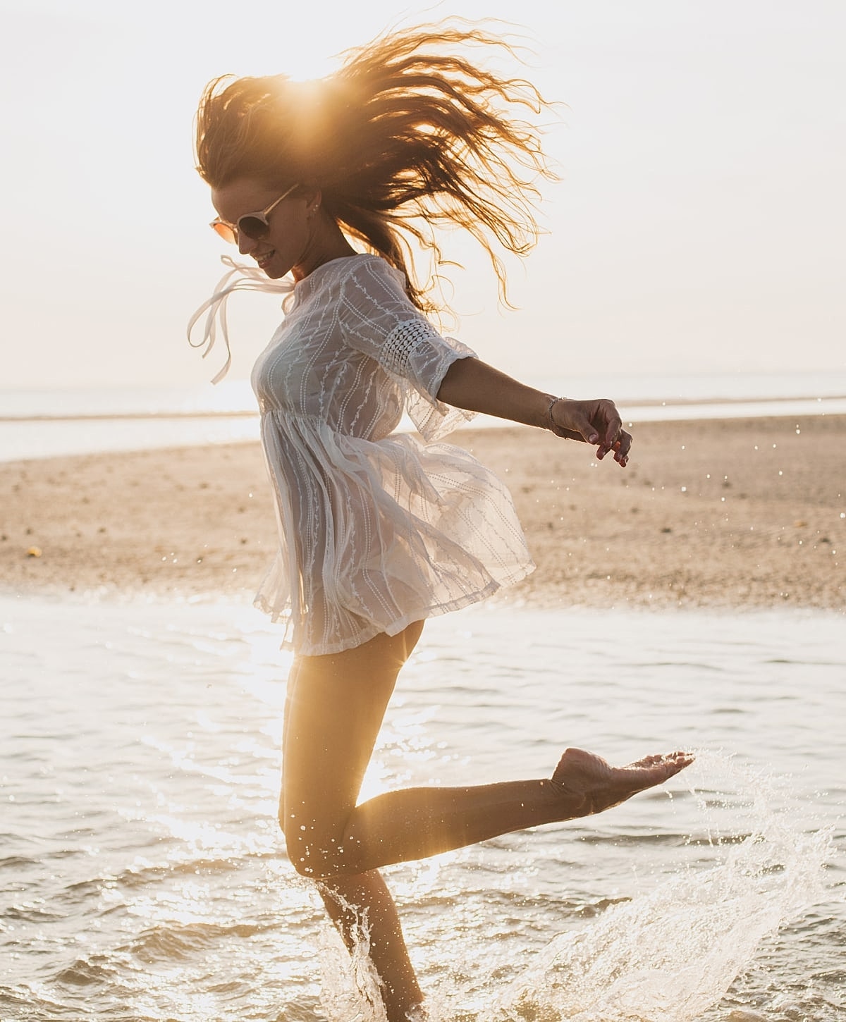 Woman playfully splashing in shallow beach water.