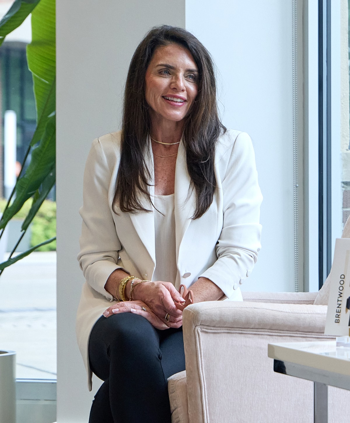 Woman smiling in stylish outfit, seated indoors.
