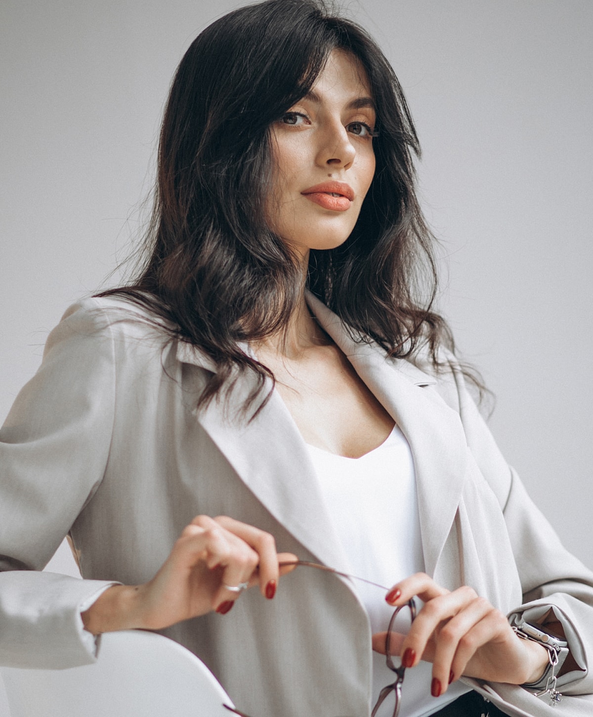 Woman in a blazer holding glasses, stylish pose.