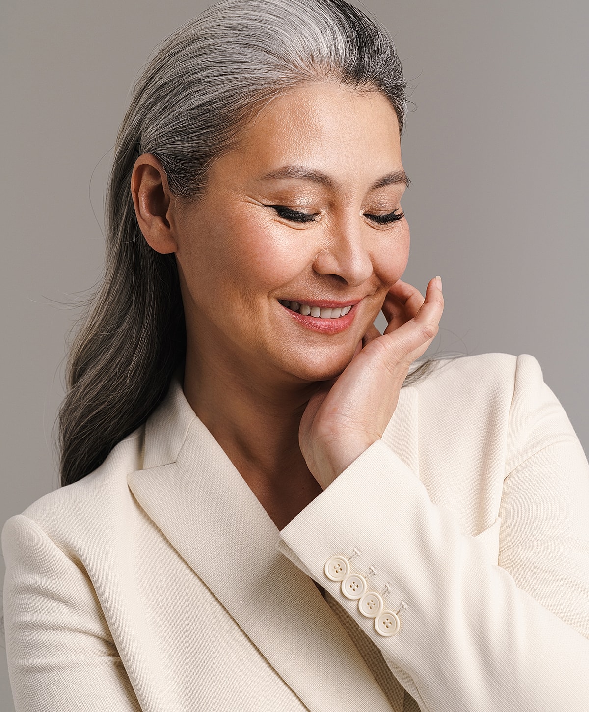 Smiling woman in cream blazer, thoughtful expression.